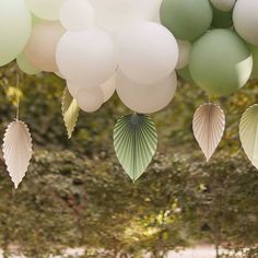 some white and green balloons are hanging from the ceiling in front of trees with leaves on them