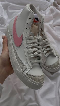 a person's hand holding a pair of white and pink nike sneakers on top of a bed