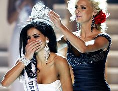 two beautiful women standing next to each other in front of a stage wearing tiaras