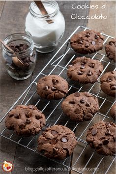 chocolate cookies are cooling on a wire rack next to a jar of milk and spoons