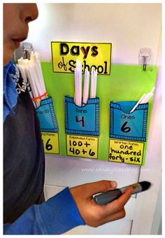 a person holding a cell phone in front of a bulletin board that says days of school