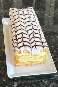 a pastry on a plate with chocolate and white icing in the shape of wavy lines