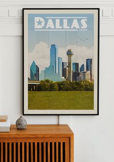 a framed poster hangs on the wall above a wooden cabinet in front of a cityscape