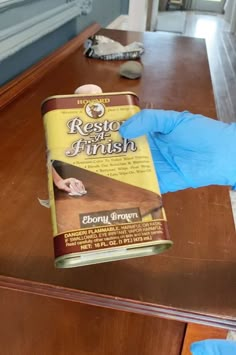 a person in blue gloves is holding a can of paint on a wooden counter top