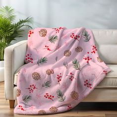 a pink blanket with pine cones and red berries on it is draped over a couch