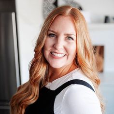 a woman with long red hair smiling at the camera while standing in front of a refrigerator