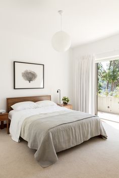 a bed sitting in a bedroom next to a window with curtains on both sides and a painting hanging above it