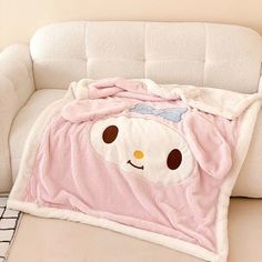 a white couch sitting next to a pink blanket on top of a pillow covered in a teddy bear face