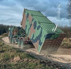 a camouflaged truck is driving down a dirt road