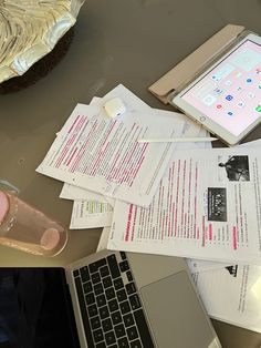 a laptop computer sitting on top of a desk next to papers and a cup filled with liquid