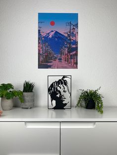 a white dresser topped with potted plants next to a painting