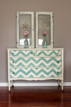 an old dresser with two mirrors on top and flowers in vases at the bottom