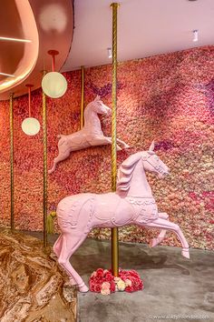 a pink horse statue sitting on top of a metal pole in front of a wall