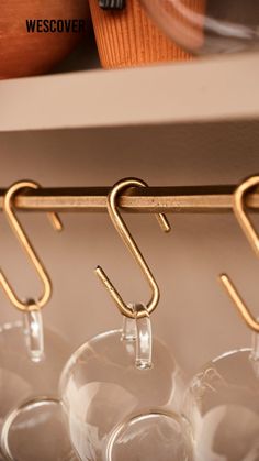 several wine glasses are hanging on a rack with gold hooks and glass holders in the background