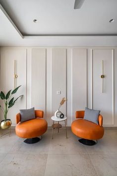 two orange chairs sitting next to each other in front of a wall with white paneling