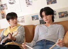 two people sitting on a couch with drums in their hands and looking at the camera