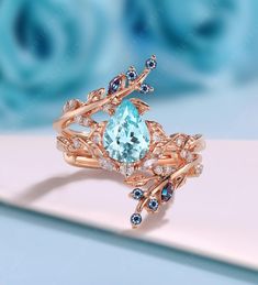 a ring with an aqua topazte surrounded by blue and white diamonds on a pink surface