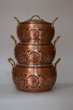 three metal bowls with gold handles and designs on them are stacked up against each other