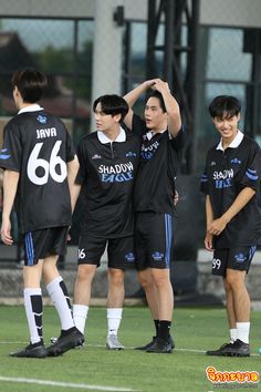 three young men standing next to each other on top of a soccer field with their hands in the air