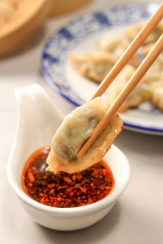 chopsticks holding up some food on a plate with dipping sauce in front of it