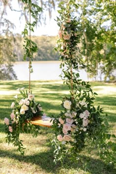 a wooden swing with flowers and greenery hanging from it's sides in the grass