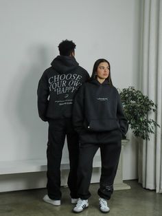 a man and woman standing next to each other wearing black hoodies with words on them