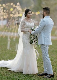 a bride and groom standing in the grass at their outdoor wedding ceremony with lights behind them