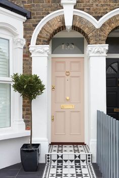 a pink front door on a brick house with black and white floor tiles, potted plant