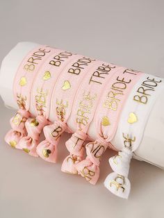 pink ribbon with gold foiled lettering and bows on the end, sitting in front of a white tube