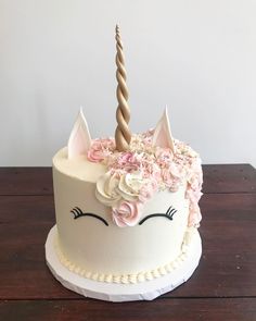 a white cake decorated with pink flowers and a unicorn's face on top is sitting on a wooden table