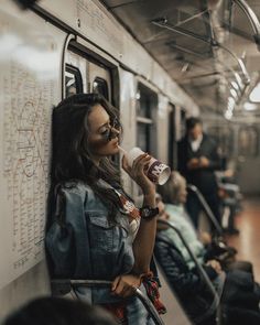 a woman drinking from a cup while standing next to a wall on a subway train