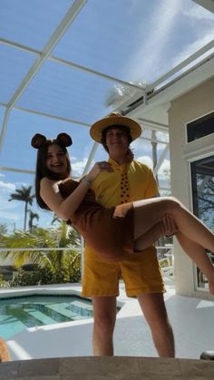 a man and woman in mickey mouse costumes standing next to a swimming pool with their arms around each other