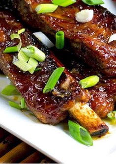 two pieces of meat sitting on top of a white plate covered in sauce and green onions