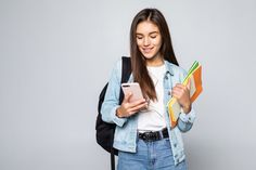 a young woman is looking at her cell phone and holding folders in one hand