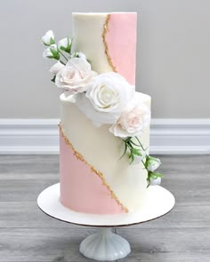 a three tiered cake with pink and white frosting, flowers on the top