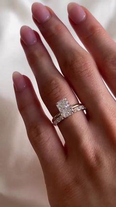 a woman's hand with a diamond ring on top of her finger and the other hand holding an engagement ring