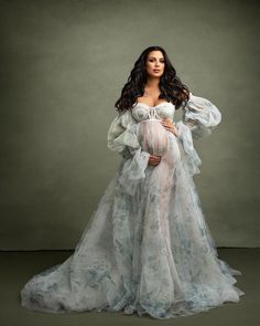 a pregnant woman in a white gown posing for the camera with her hands on her hips