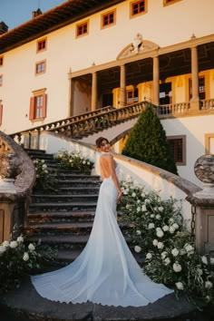 a woman in a wedding dress standing on the steps of a building with white flowers