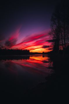 the sun is setting over a lake with trees in the foreground and clouds in the background