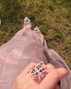 a woman's hand is holding an engagement ring in front of her feet on the grass