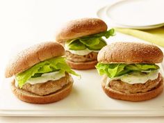 three sandwiches with lettuce and mayonnaise are on a white platter