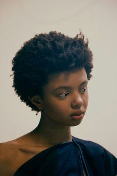 a woman with an afro is looking at her cell phone while wearing a blue top