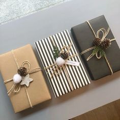 three wrapped presents sitting on top of a table next to pine cones and twine