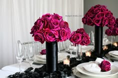 the table is set with black and white plates, silverware, and pink roses