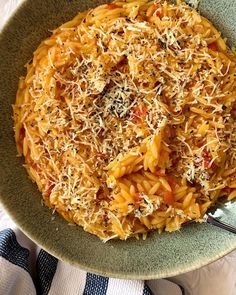 a green bowl filled with pasta and cheese on top of a white table cloth next to a fork