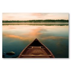 a boat is sitting on the water at sunset with fog in the sky above it