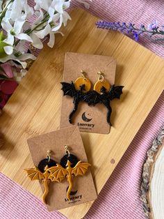 two bat shaped earrings sitting on top of a wooden board