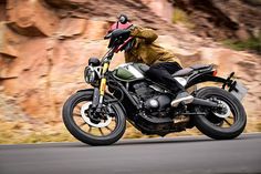 a man riding on the back of a motorcycle down a road next to a mountain