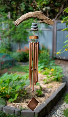 a wind chime hanging from a tree branch in a garden with rocks and wood