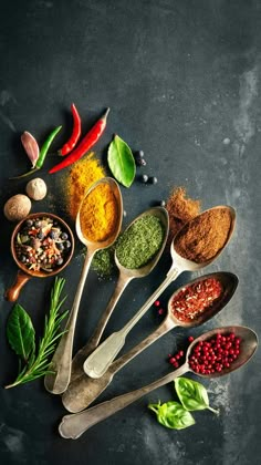 spoons filled with different types of spices and herbs on a dark background, top view